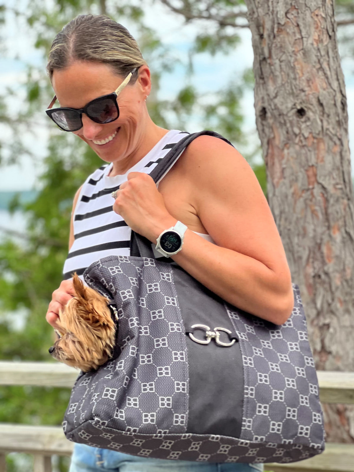 Dog being carried in a dark signature-pattern pet tote with top handle and front clasp