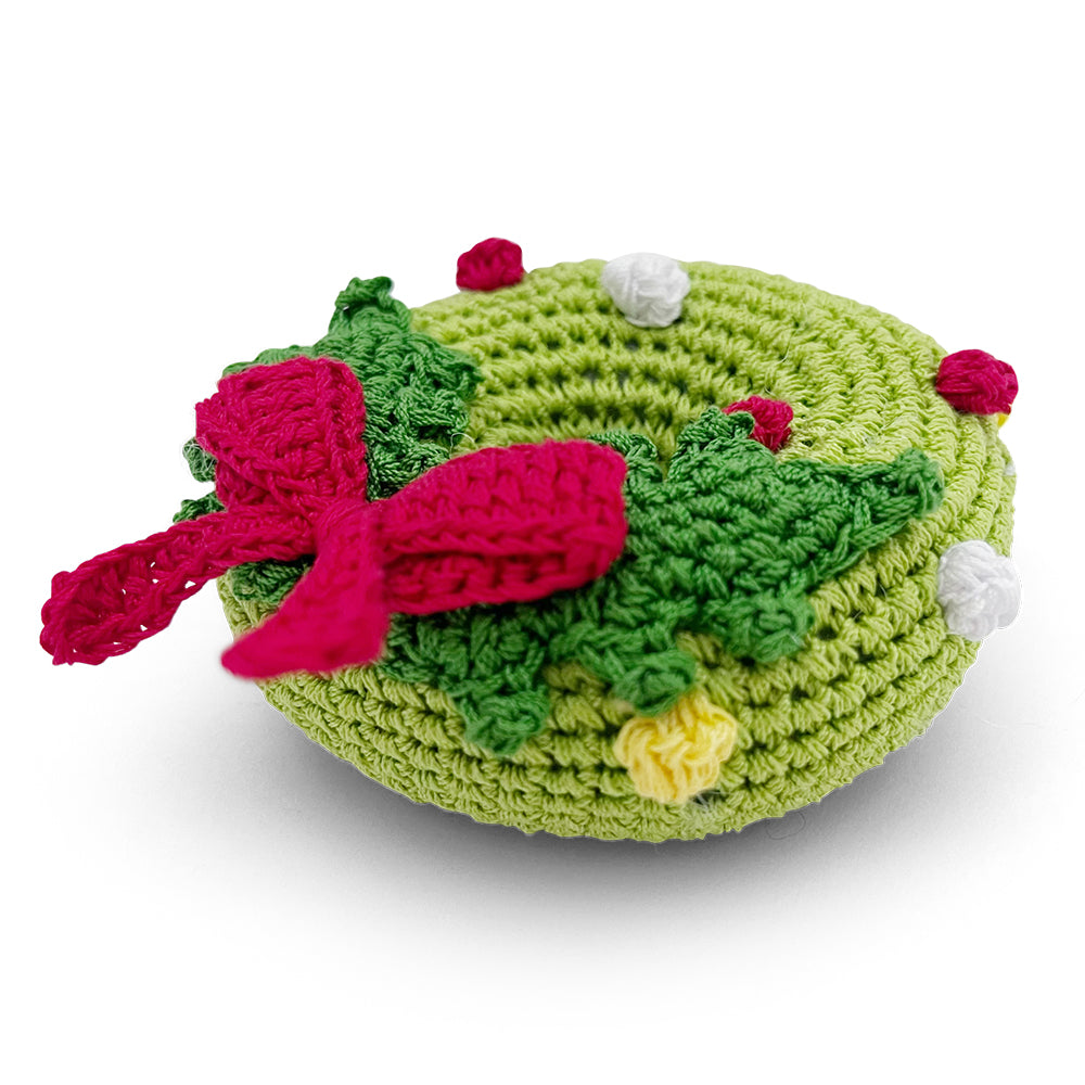 Crochet wreath dog toy with green body, red bow, and small white and yellow details