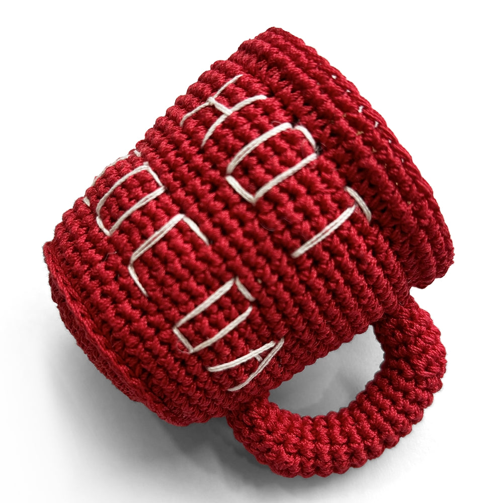 Red crochet dog toy mug with white stitched cocoa pattern and loop handle, side view