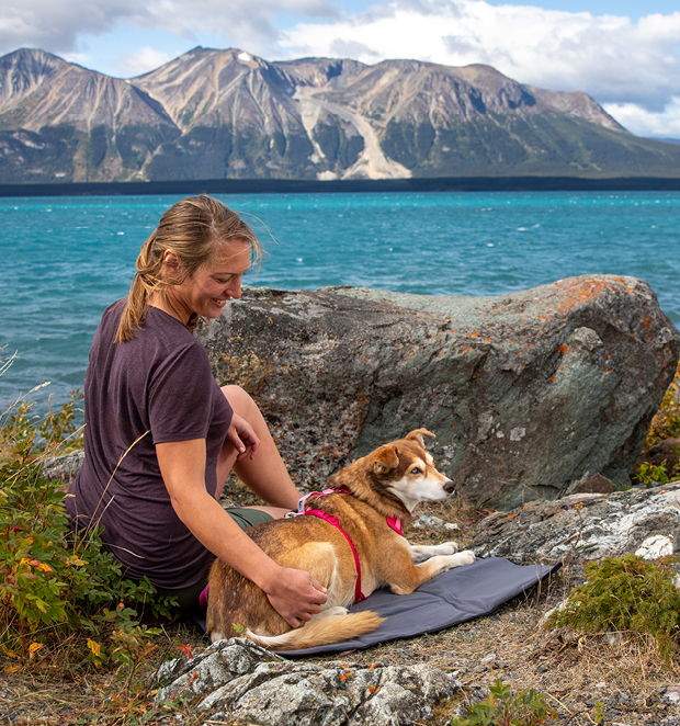 Gray dog travel mat on rocky ground with dog relaxing on the padded surface