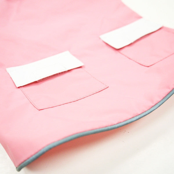 Pink dog raincoat with front tabs and teal-edged hem, laid flat