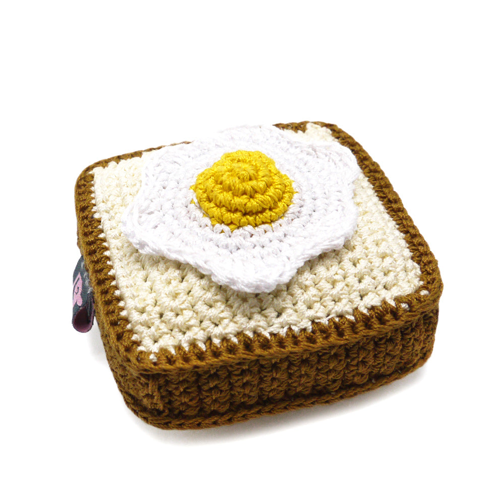Crochet dog toy with squeaker, brown square base and white egg with yellow yolk, angled view