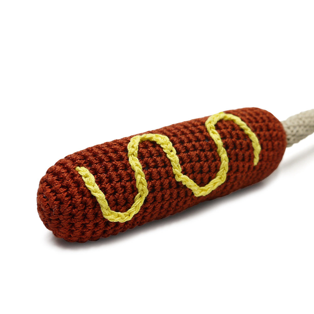 Crocheted dark brown hot dog toy with yellow wavy lines and light gray rope-like tail